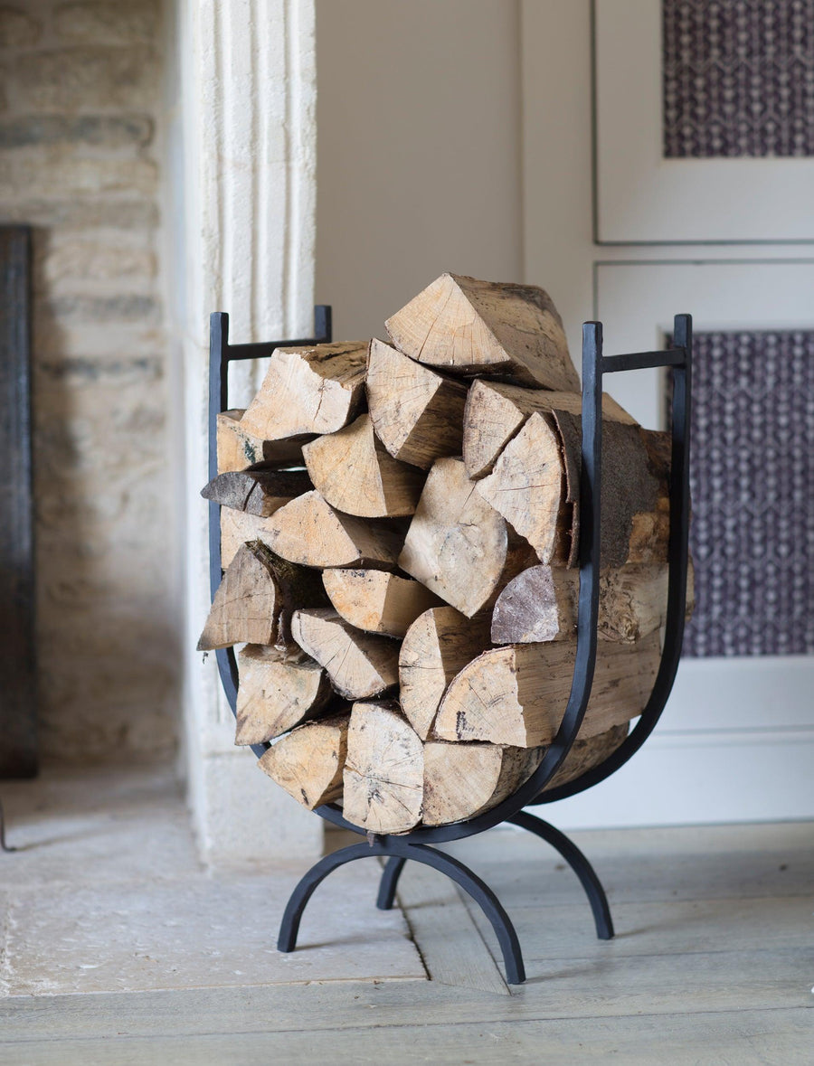 Wooden logs stacked on a metal firewood holder in a room with a fireplace.