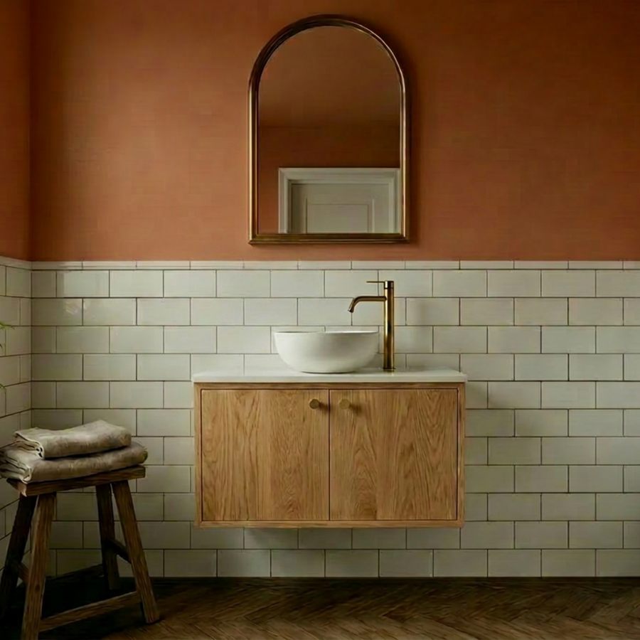 Oak Wall Hung Vanity Unit with Doors with a white oval sink, gold faucet, light wood cabinet, white subway tile wall, and an arched mirror against a terracotta-colored wall.