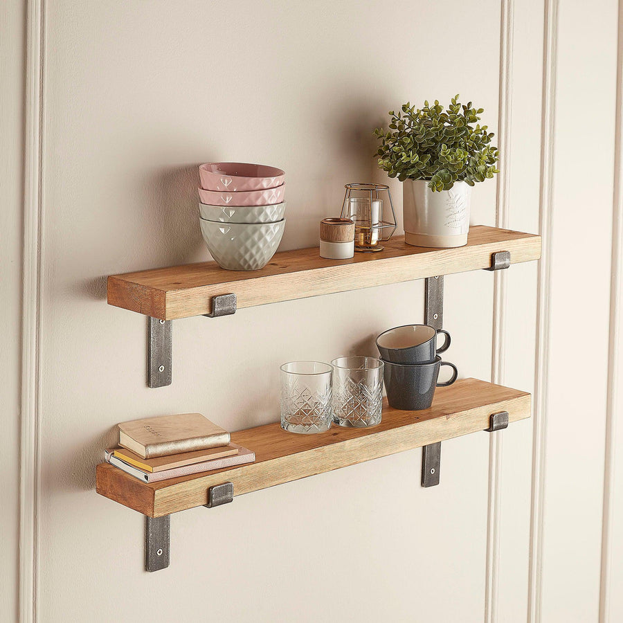 Narrow rustic wooden shelf with metal brackets mounted on a wall and styled with bowls, mugs and plants