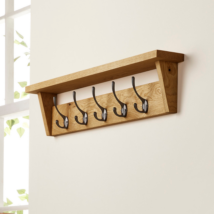 walnut coat rack with shelf, five black metal hooks mounted on a wall.