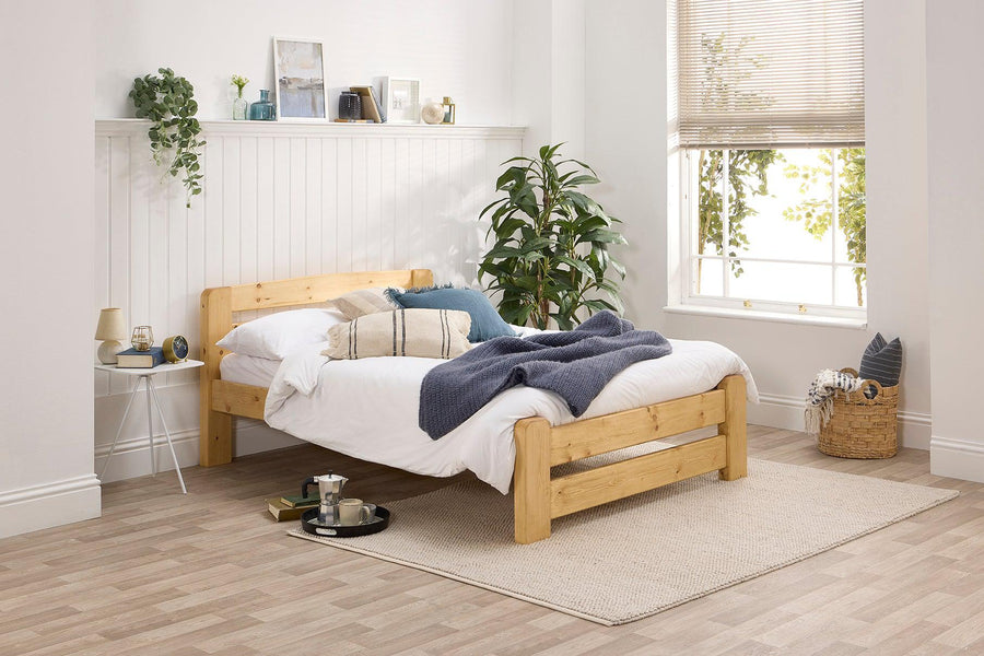 A wooden bed frame with a headboard and footboard, in a rustic style, painted in a natural wood color, placed in a bedroom setting with bedding and decorative pillows.