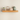 A floating wooden radiator shelf mounted on a beige wall, styled with a small potted succulent, a gold wire lantern, a ribbed pink ceramic box, and a textured sage green decorative egg.