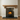 Solid oak corbel supporting the fireplace shelf, with a glowing fire inside, set within a white fireplace surround with a rustic wooden mantel and a dark hearth plate on a wood floor.