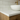 A close-up of an oak wall hung vanity featuring a white countertop, a white vessel sink, a brushed gold faucet, and light wood cabinetry against a white subway tile backsplash.
