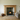 Wood-burning stove in a living room with a wooden fireplace mantle, rug, and sofa.