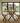 side view of solid pine dining table and bench set with x frame legs with benches in a room with large glass doors leading to a garden.
