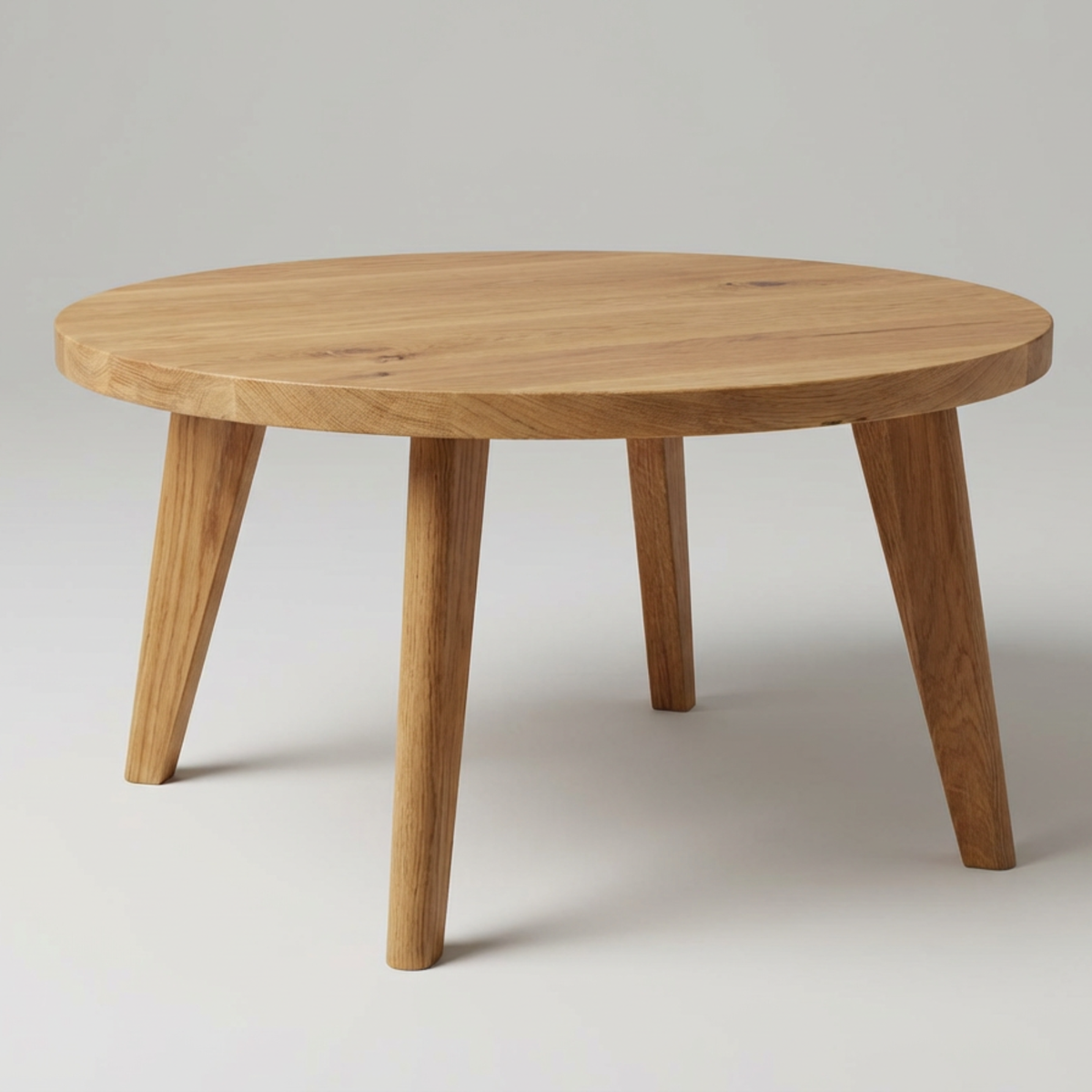 Round solid oak coffee table with four legs on a plain background