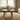 Round oak coffee table in a living room with books and a vase on top, near a window with curtains.