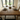 oak dining table and bench set with A frame legs set with plates, glasses, and a small plant in a room with large windows.