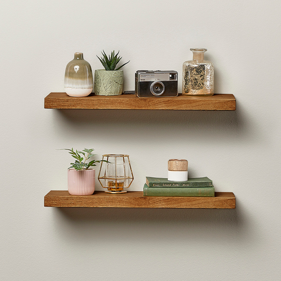 Two walnut floating shelves mounted on a wall, styled with plants, books and decor.