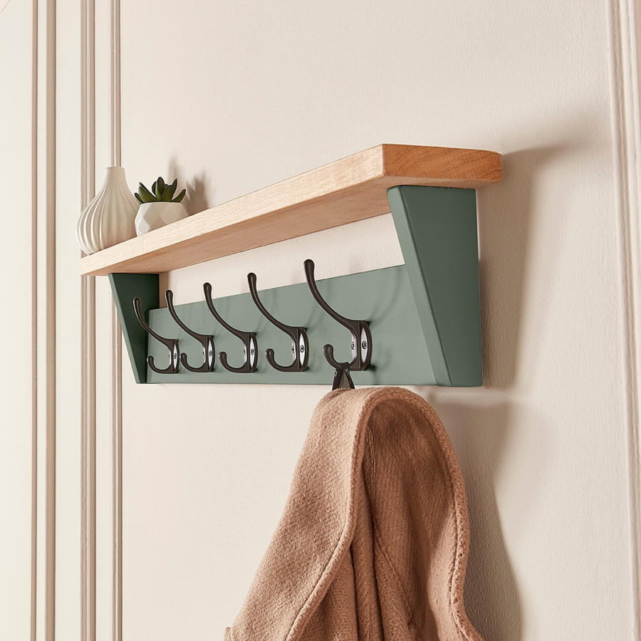 Green Smoke coat rack with shelf wall mounted, showing a coat hanging from black hooks and ornaments styled on the wooden shelf