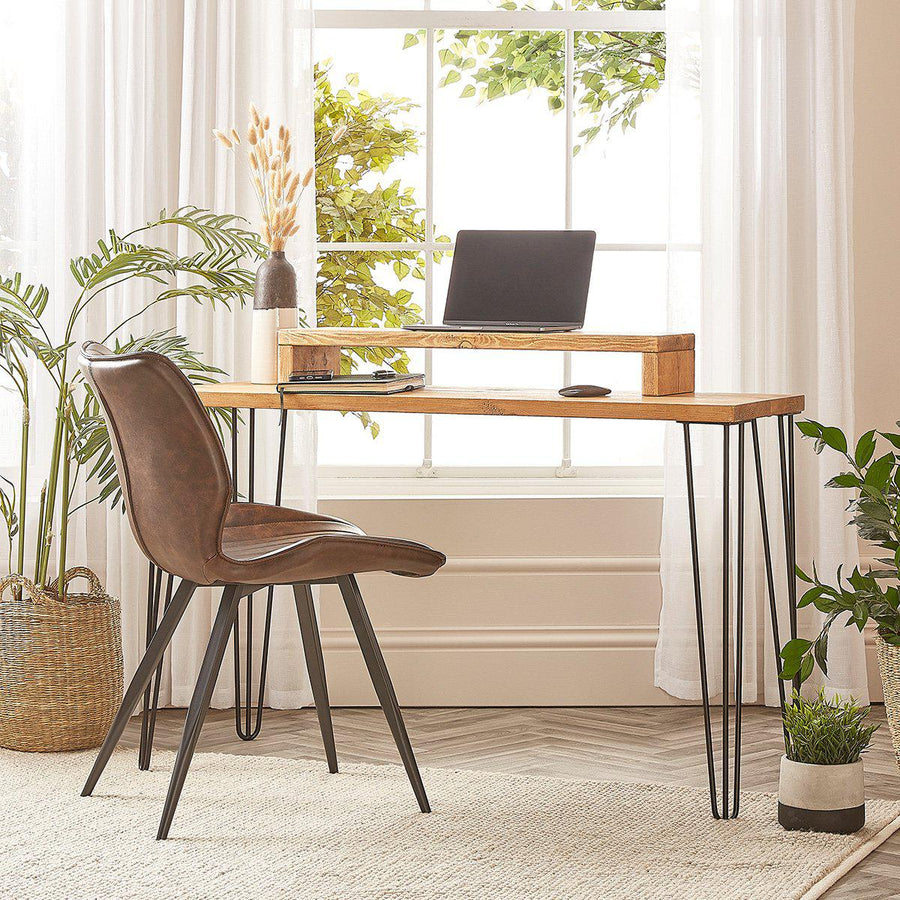 A reclaimed wooden computer desk with four sturdy steel hairpin legs, positioned in an office setting with a laptop on top and surrounded by plants and a chair.