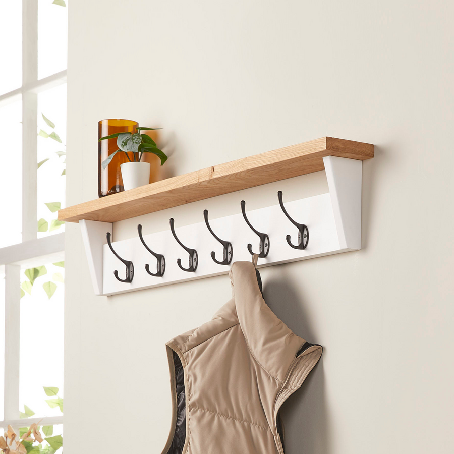 White painted wooden coat rack with oak shelf mounted on wall, showing coat hanging from metal hook